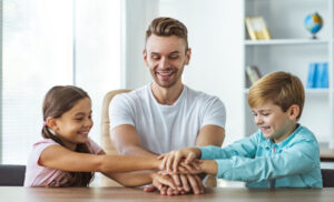 The happy father with kids hold hands together at the table