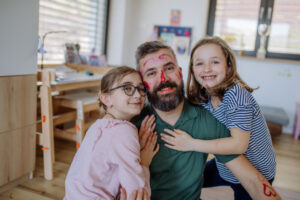 Two little girls putting on make up on their father, fathers day with daughters at home.